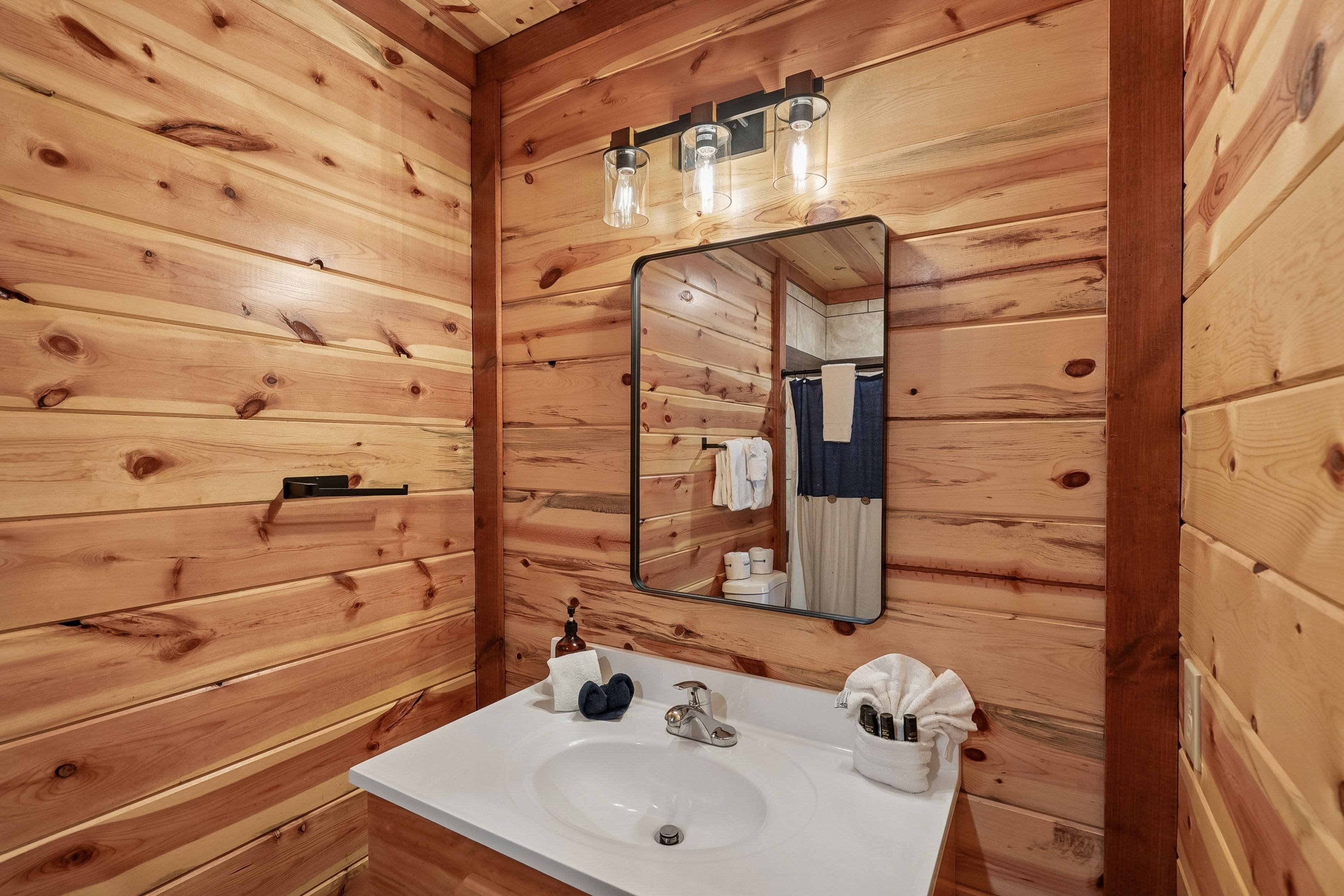 Ein Badezimmer mit Holzwandverkleidung, einem weißen Waschbecken, einem Spiegel und einem Handtuchhalter.