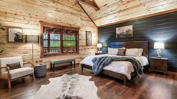 A log cabin bedroom with a bed, a bench, a cowhide rug, and a window with blinds.