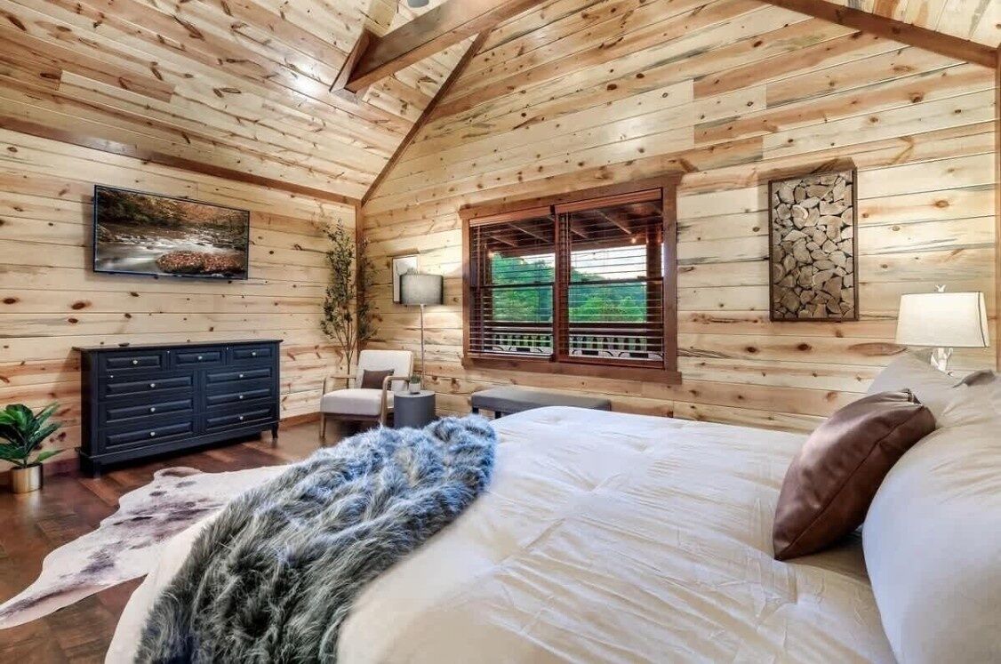 A wooden cabin interior with a bed, dresser, and window.