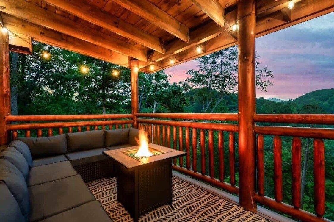 A wooden deck with a built-in fire feature, seating, and a view of a forested landscape.