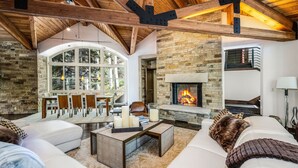 A cozy living room with a fireplace, stone walls, and a dining area with natural light. - For486 5 Bedroom Home (Vail)