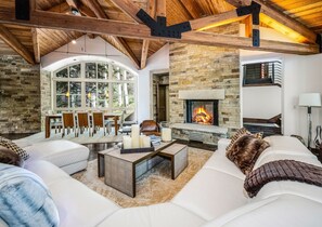 A cozy living room with a fireplace, stone walls, and a dining area with natural light. - For486 5 Bedroom Home (Vail)