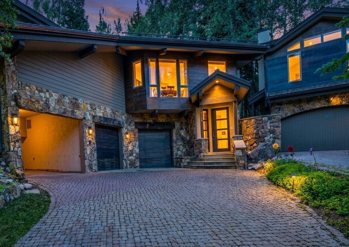 Une maison à deux étages avec une façade en pierre, un porche à l’avant et une allée menant à un garage.
