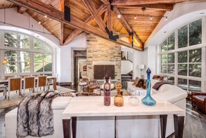 A spacious living area with a high ceiling, large windows, and a fireplace. - For486 5 Bedroom Home (Vail)