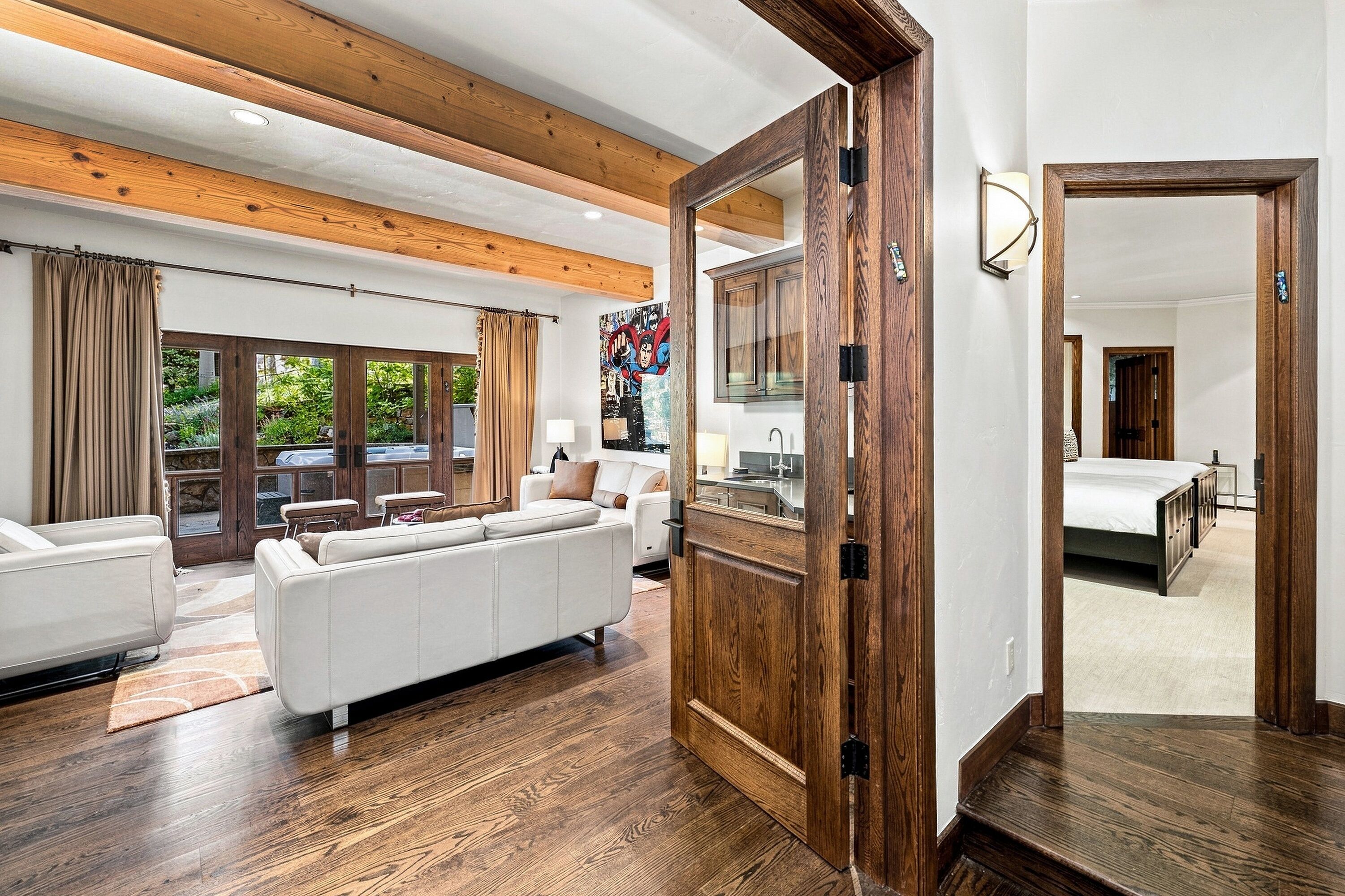 A spacious living area with a white sofa, wooden flooring, and a large wooden door leading to another room.