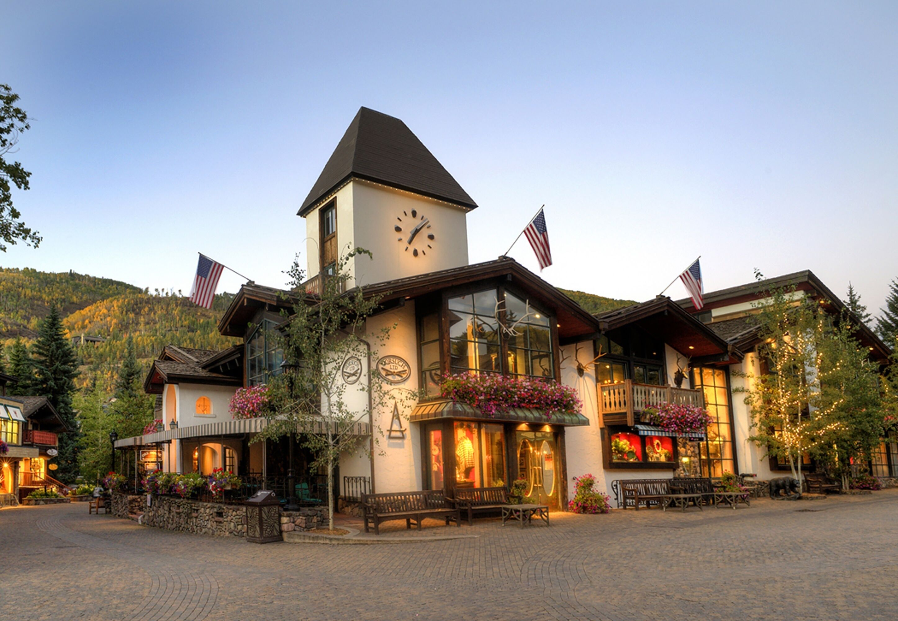 A hotel with a prominent clock tower, multiple flags, and a welcoming entrance with benches and flower arrangements.