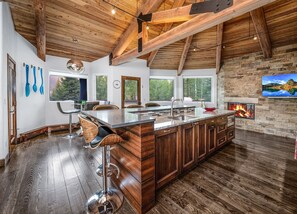 A modern kitchen with a large island, wooden beams, stone walls, and a fireplace. - For486 5 Bedroom Home (Vail)