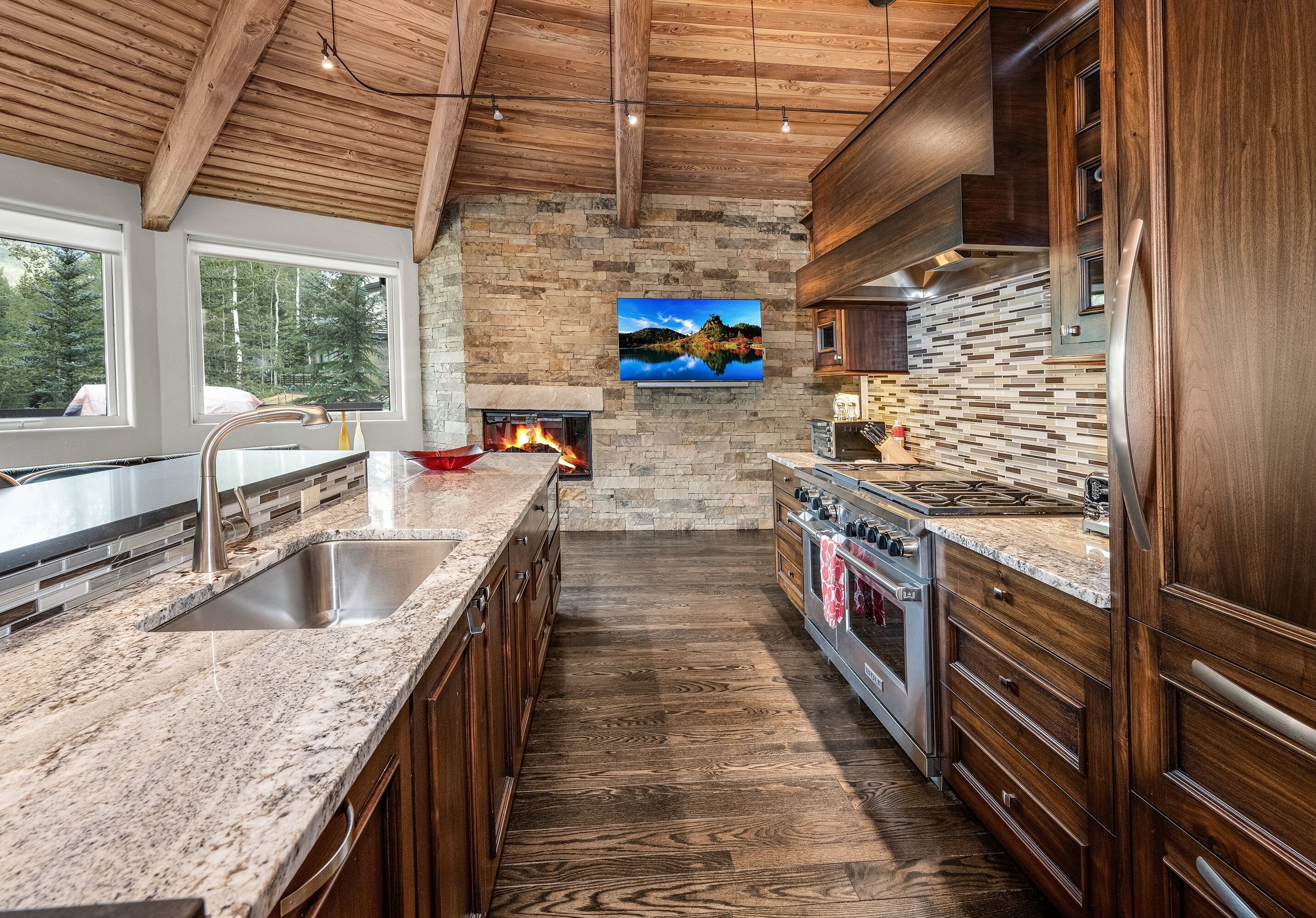 A kitchen with a stone fireplace, wooden cabinets, and a large island with a sink.