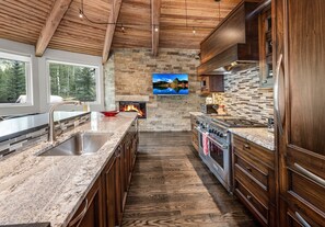 A kitchen with a stone fireplace, wooden cabinets, and a large island with a sink. - For486 5 Bedroom Home (Vail)