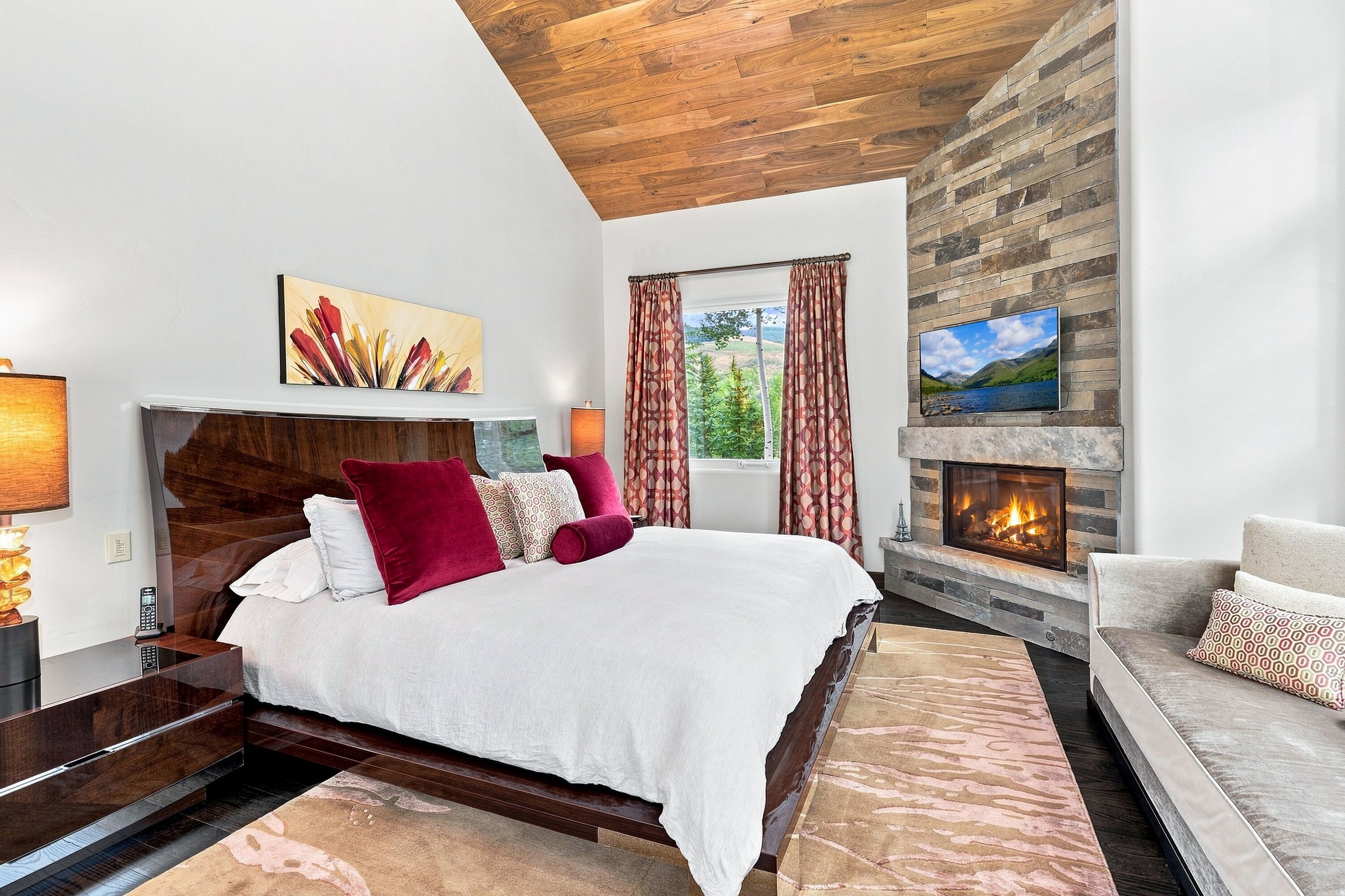 A bedroom with a bed, a fireplace, a television, and a window with curtains.