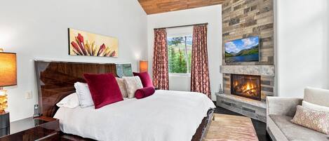 A bedroom with a bed, a fireplace, a television, and a window with curtains.