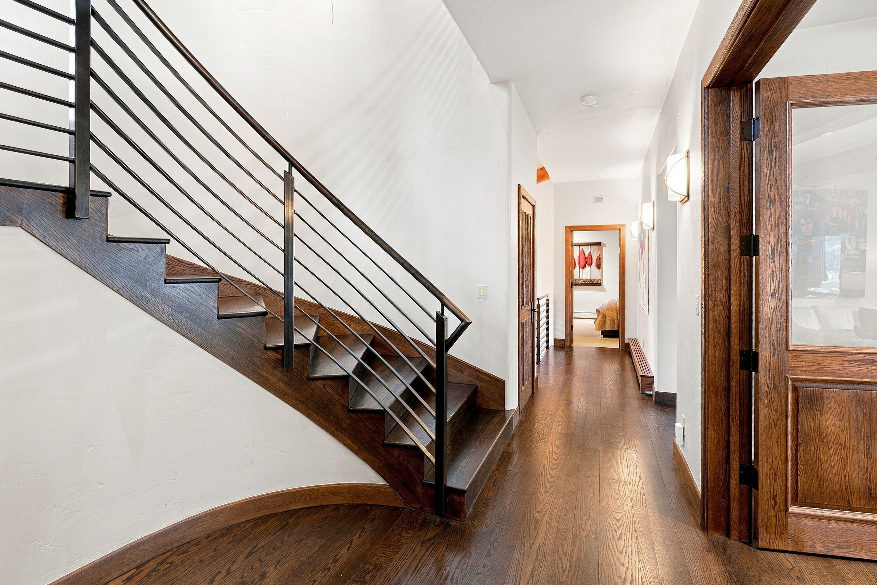 A staircase with a wooden finish and metal railings leading to a hallway with wooden flooring and a door with glass panels.