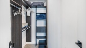 A narrow walk-in closet with wooden shelving, a hanging rack, and a bed with a pillow. - 17th floor skyline retreat in Downtown Miami rooftop pool, coworking lounge and self check-in (Miami)