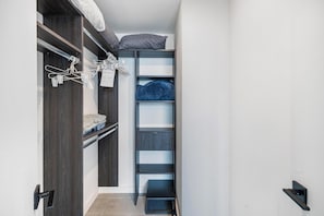 Ein schmaler begehbarer Kleiderschrank mit Holzböden, einer Kleiderstange und einem Bett mit Kissen.