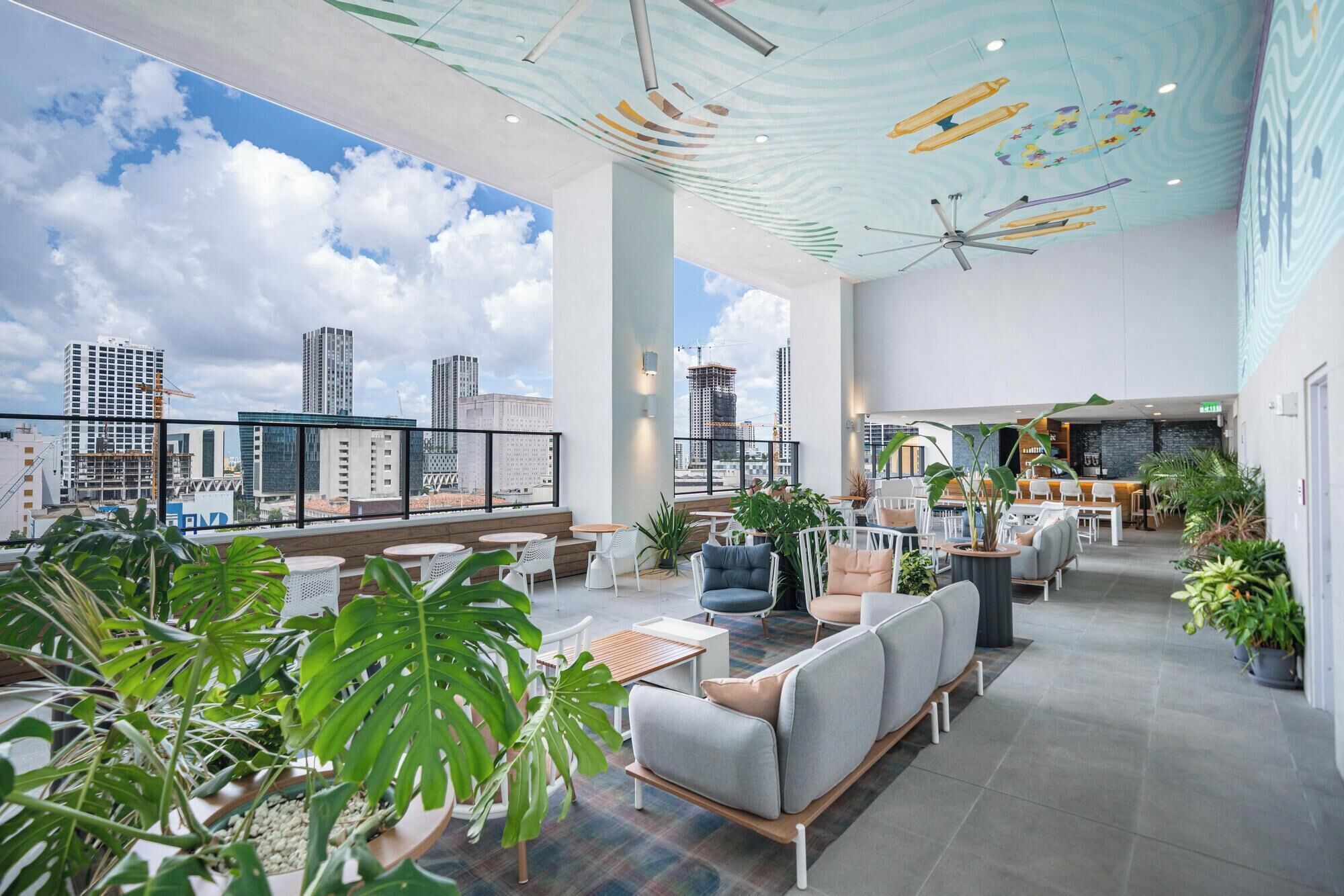 A modern hotel lobby with a city view, large windows, and a ceiling with a unique design.