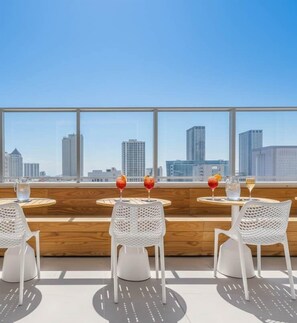 A rooftop bar with three white chairs and tables, each with a drink and a glass. The view includes tall buildings in the distance. - 17th floor skyline retreat in Downtown Miami rooftop pool, coworking lounge and self check-in (Miami)