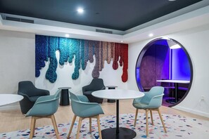 A modern lounge area with a round table and chairs, a colorful wall art installation, and a unique circular seating area with blue lighting. - 17th floor skyline retreat in Downtown Miami rooftop pool, coworking lounge and self check-in (Miami)
