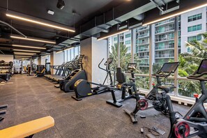 A gym with various exercise equipment, large windows, and a view of a building outside. - 17th floor skyline retreat in Downtown Miami rooftop pool, coworking lounge and self check-in (Miami)