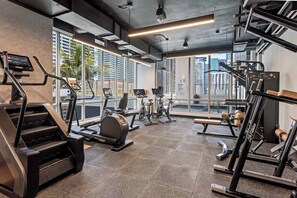 A modern gym with various exercise equipment, large windows, and a city view. - Skyline Studio w/ Pool & Gym | Walk to Bayside (Miami)