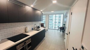 A modern kitchen with dark cabinets, a white countertop, and a large window. - Skyline Studio w/ Pool & Gym | Walk to Bayside (Miami)