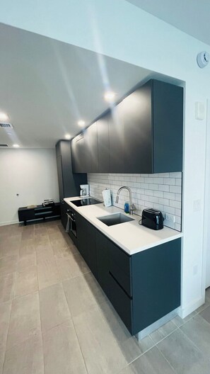 A modern kitchen with a white countertop, dark cabinets, and a tiled backsplash. - Skyline Studio w/ Pool & Gym | Walk to Bayside (Miami)