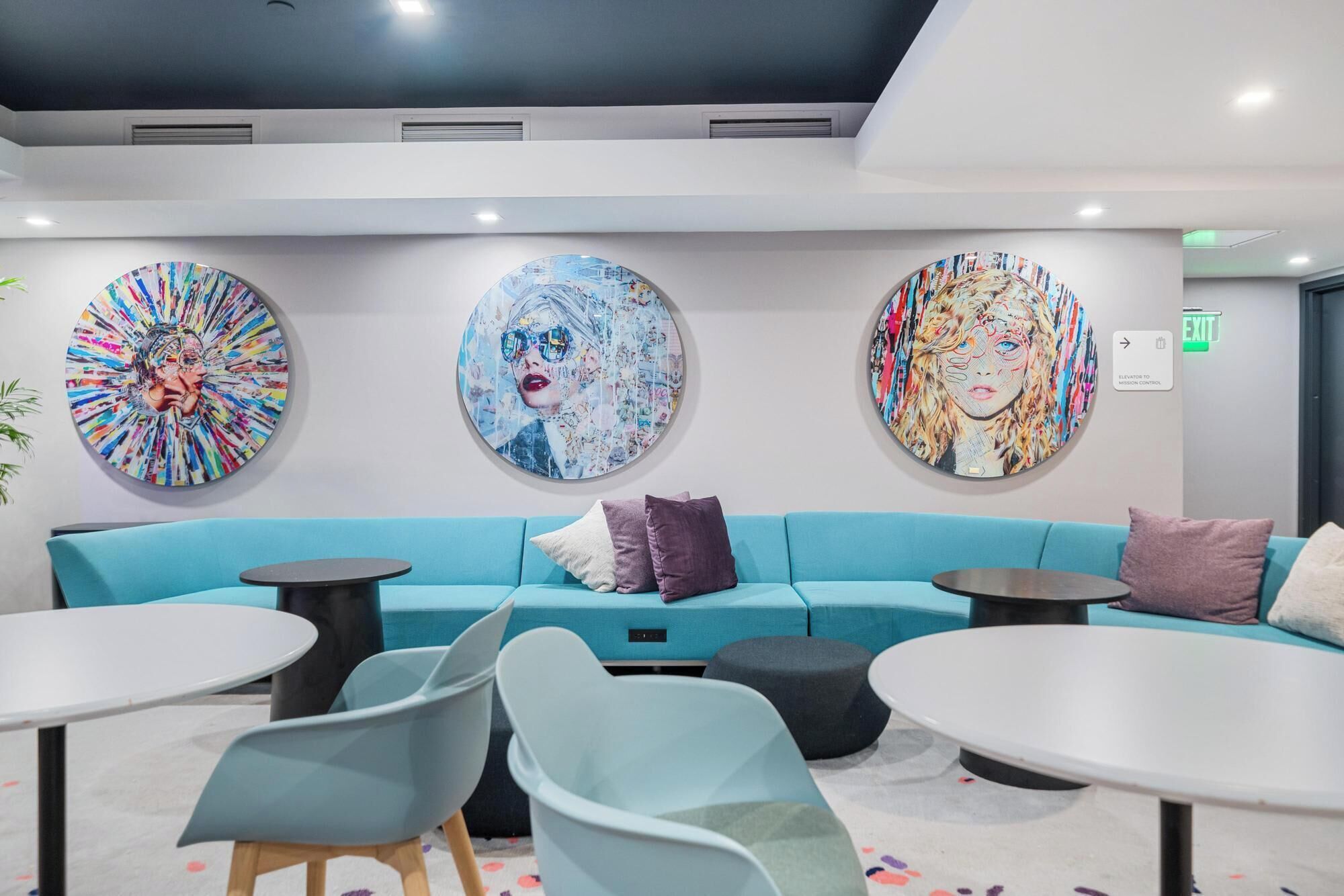 Un espace de détente moderne avec un canapé de couleur turquoise, des tables rondes et trois grandes œuvres d’art circulaires accrochées au mur.