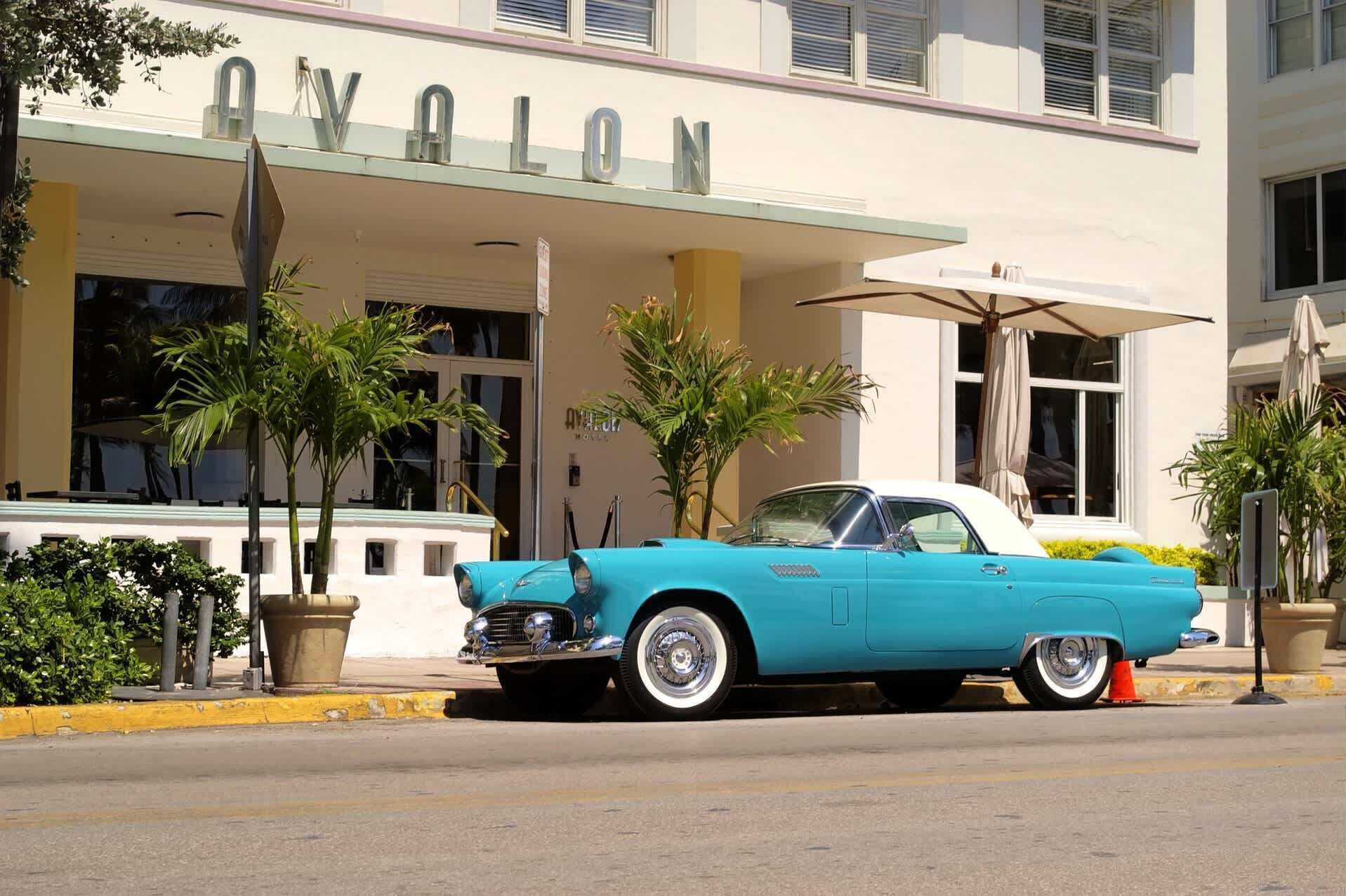 A vintage turquoise car parked in front of a building with a 'V' sign.