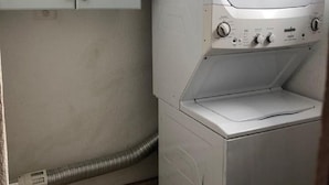Een kleine wasruimte met een voorlader wasmachine en een droger, een lichtblauwe kast erboven, en een zichtbare slang.