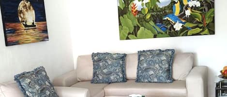 A living room with a sofa, armchairs, a coffee table, a ceiling fan, and two wall-mounted paintings.