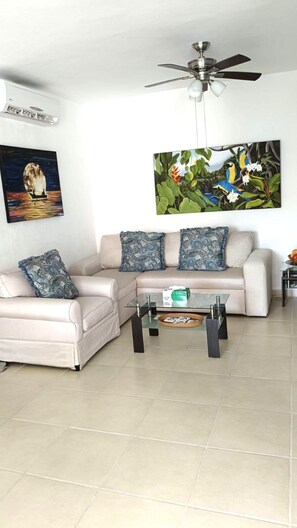 A living room with a sofa, armchairs, a coffee table, a ceiling fan, and two wall-mounted paintings. - P. H. PRIVATE PATIO W/ THERMO TUB./POOL, 1 BLK TO RESTRNT & MRKT, CLOSE TO BEACH (Playa del Carmen)