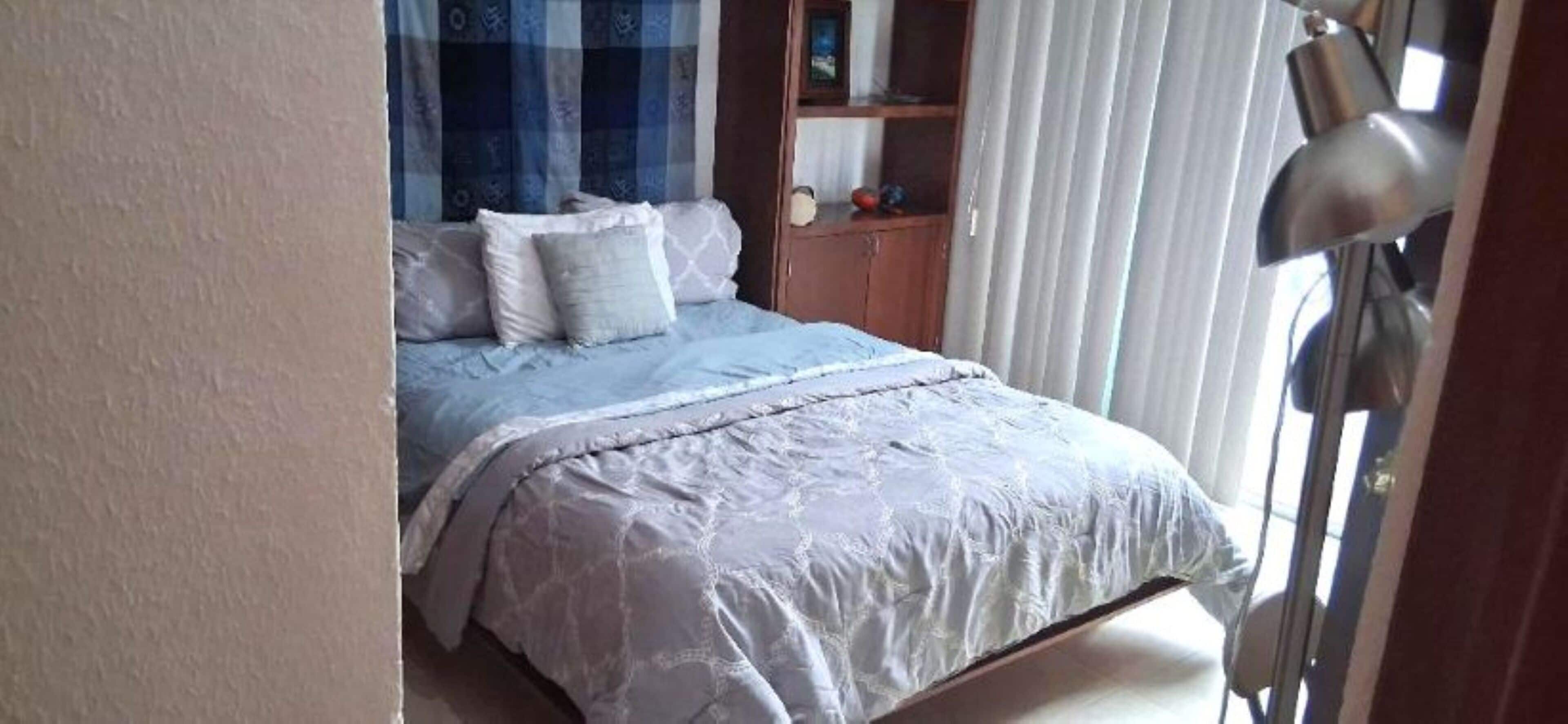 A bedroom with a bed, a nightstand, a lamp, and a window with curtains.