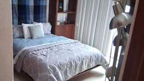 Een slaapkamer met een bed, nachtkastje, lamp en een raam met gordijnen.