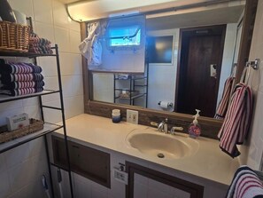 Een badkamer met een wastafel, spiegel, handdoekrek en planken met opgevouwen handdoeken en een mandje.