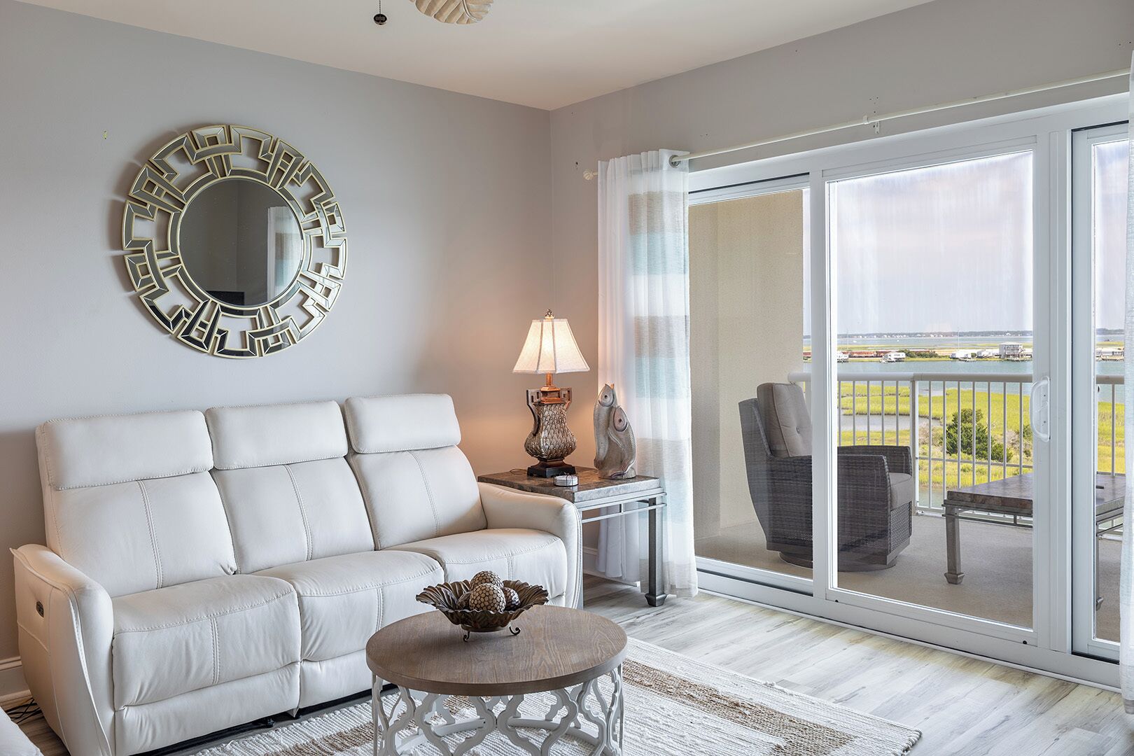 Un salon avec un canapé blanc, une table ronde sur laquelle se trouve un saladier, une lampe et un grand miroir accroché au mur.
