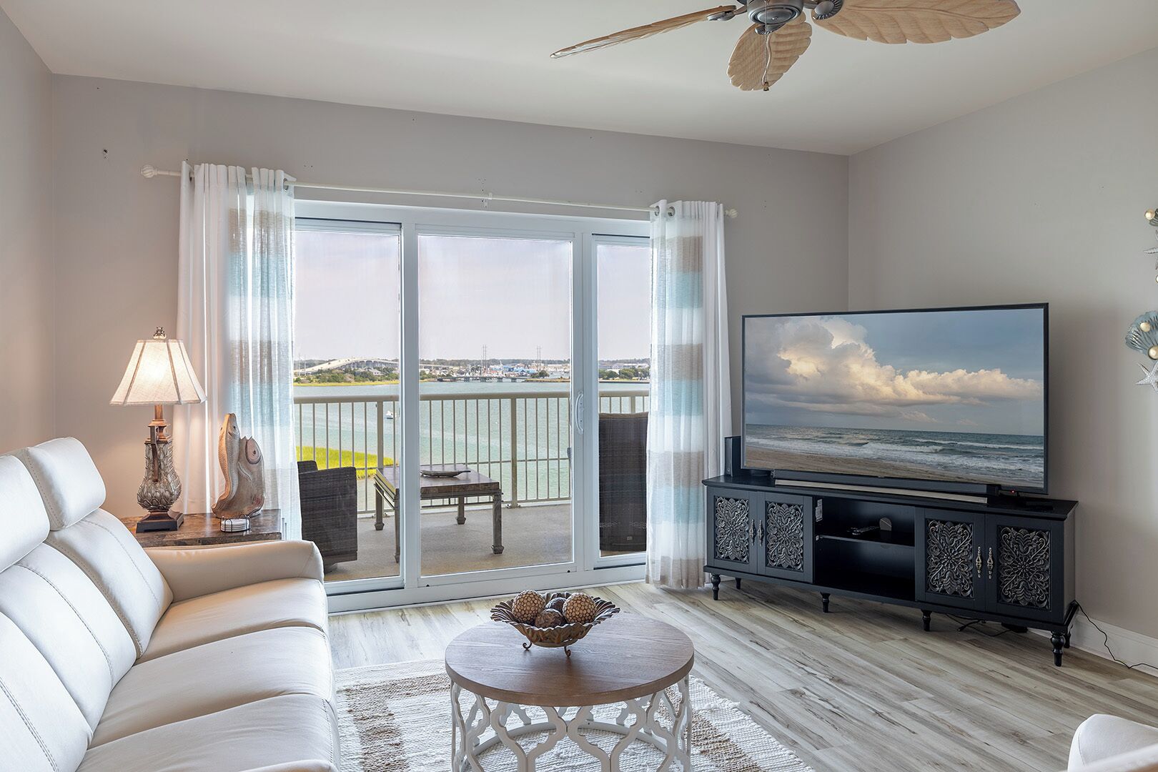 Een woonkamer met een bank, een televisie, een salontafel en een balkon met uitzicht op zee.
