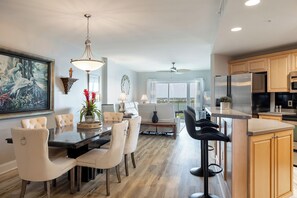A modern kitchen with a central island, wooden cabinets, and a dining area with a large painting and a vase of flowers. - Olde Towne Yacht Club 512 (Beaufort)