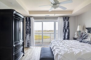 A bedroom with a large bed, a wardrobe, a ceiling fan, a view of a body of water, and a balcony with curtains. - Olde Towne Yacht Club 512 (Beaufort)