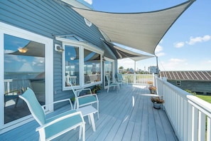 A covered outdoor deck with white railings, seating, and potted plants. - Amazing BAY VIEWS at Moon Fish by Seaside Vacations! (Chincoteague Island)