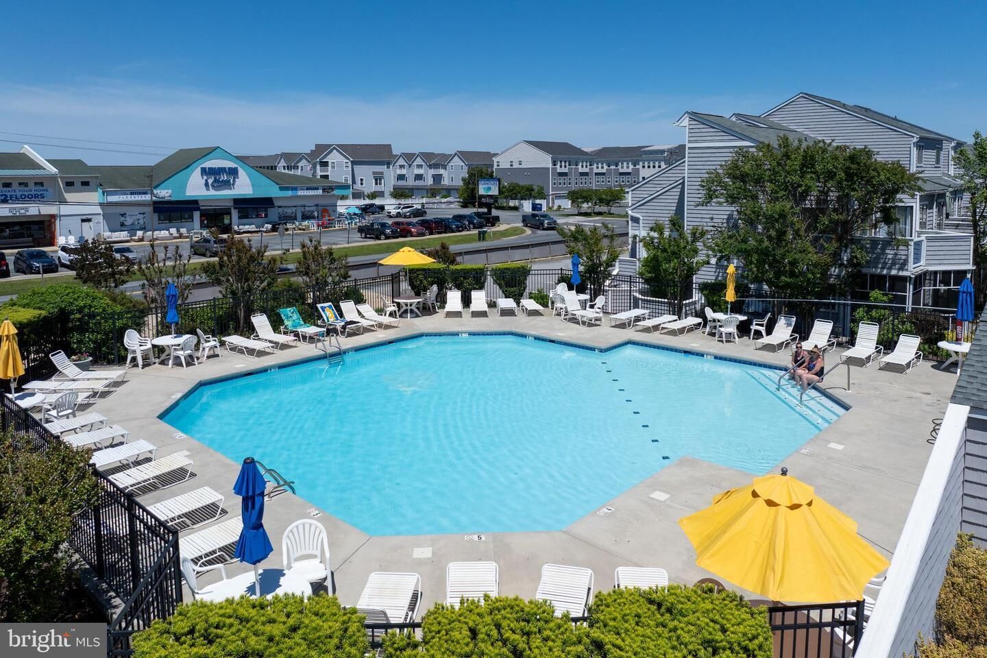 A swimming pool with lounge chairs and umbrellas, surrounded by residential buildings.