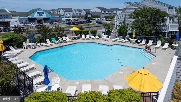 A swimming pool with lounge chairs and umbrellas, surrounded by residential buildings. - East of the Sun 39866 E Sun Dr 327 (Fenwick Isle)