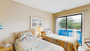 Ein Hotelzimmer mit zwei Betten, einem Fenster mit Außenblick, einem Gemälde an der Wand und einer Lampe auf einem Nachttisch.