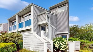 A two-story residential building with a modern design, featuring a prominent staircase and a well-maintained garden with various plants and flowers. - East of the Sun 39866 E Sun Dr 327 (Fenwick Isle)