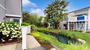 Zona residencial con un estrecho canal, céspedes cuidados y árboles maduros.
