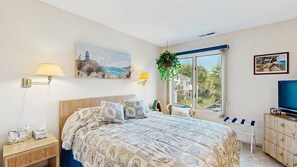 A bedroom with a bed, bedside lamps, a TV, a window with a view, and a painting on the wall. - East of the Sun 39866 E Sun Dr 327 (Fenwick Isle)