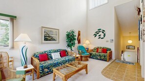 Ein Wohnzimmer mit Sofa, Sessel und Couchtisch, einem Bild an der Wand und einer Pflanze.