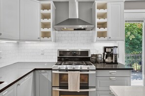 Una cocina moderna con estufa de acero inoxidable, armarios blancos y una campana extractora empotrada.