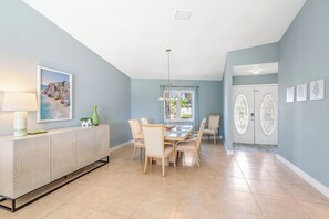 A dining area with a table and chairs, a cabinet with decorative patterns, and a painting on the wall. - Tropical Shores St Pete Waterfront Pool (St Petersburg)