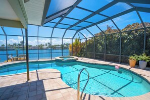 Une piscine intérieure offrant une vue dégagée sur le paysage environnant, notamment sur une étendue d’eau et des palmiers.