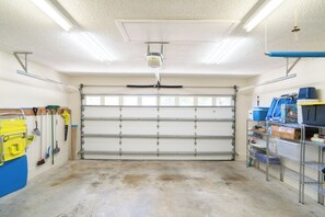 A garage with a closed garage door, overhead fluorescent lighting, a ceiling fan, and various cleaning tools and supplies on shelves. - Tropical Shores St Pete Waterfront Pool (St Petersburg)