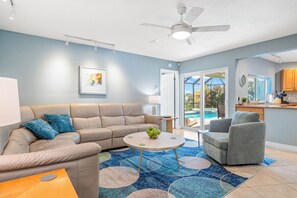 A modern living room with a beige sectional sofa, a grey armchair, a coffee table with a fruit bowl, and a ceiling fan. - Tropical Shores St Pete Waterfront Pool (St Petersburg)